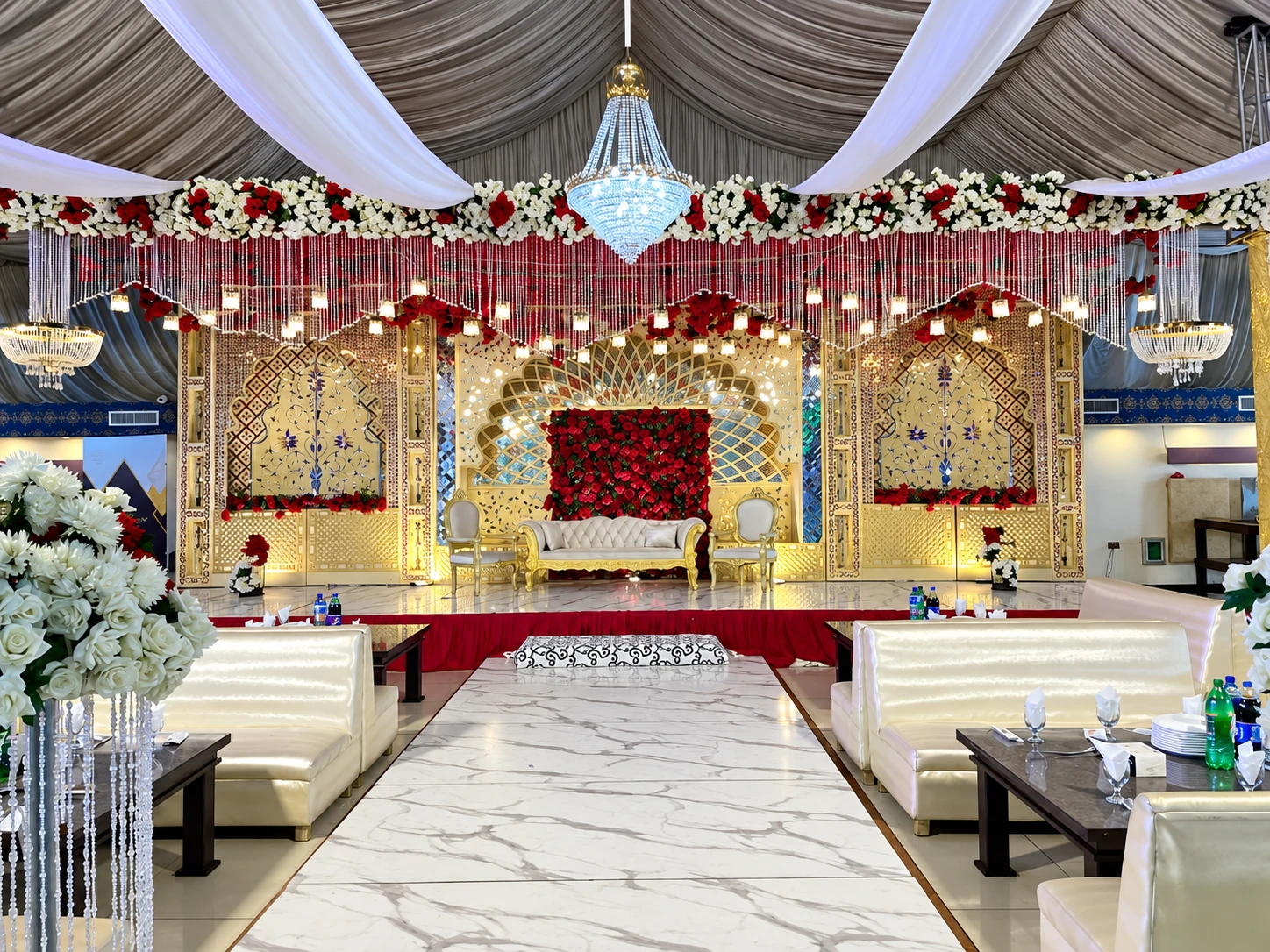 Gold jali wedding stage with red floral wall and crystal chandelier at Al Hassan Grand Marquee