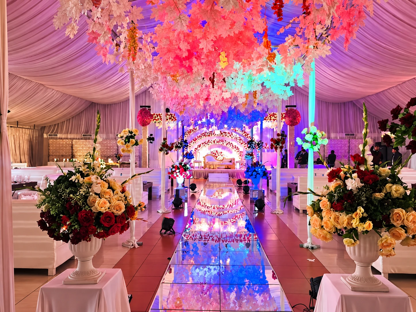 Hanging floral canopy with colourful lighting over a mirror walkway